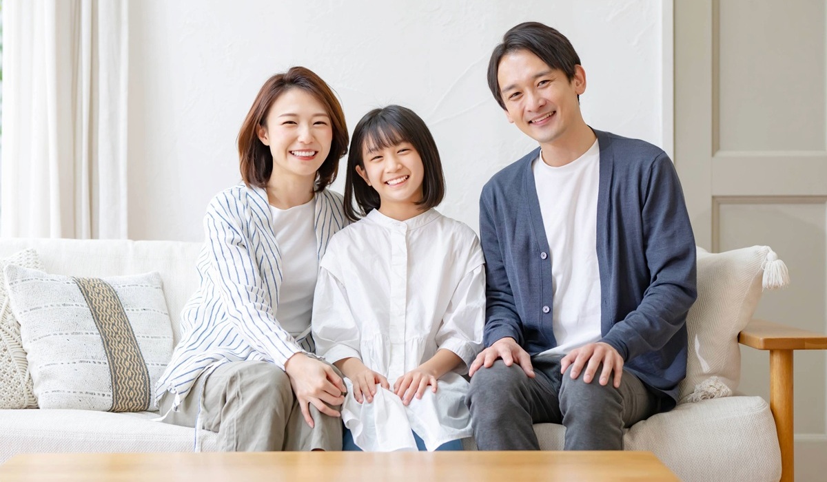 自宅のソファで笑顔で座る家族（両親と娘）