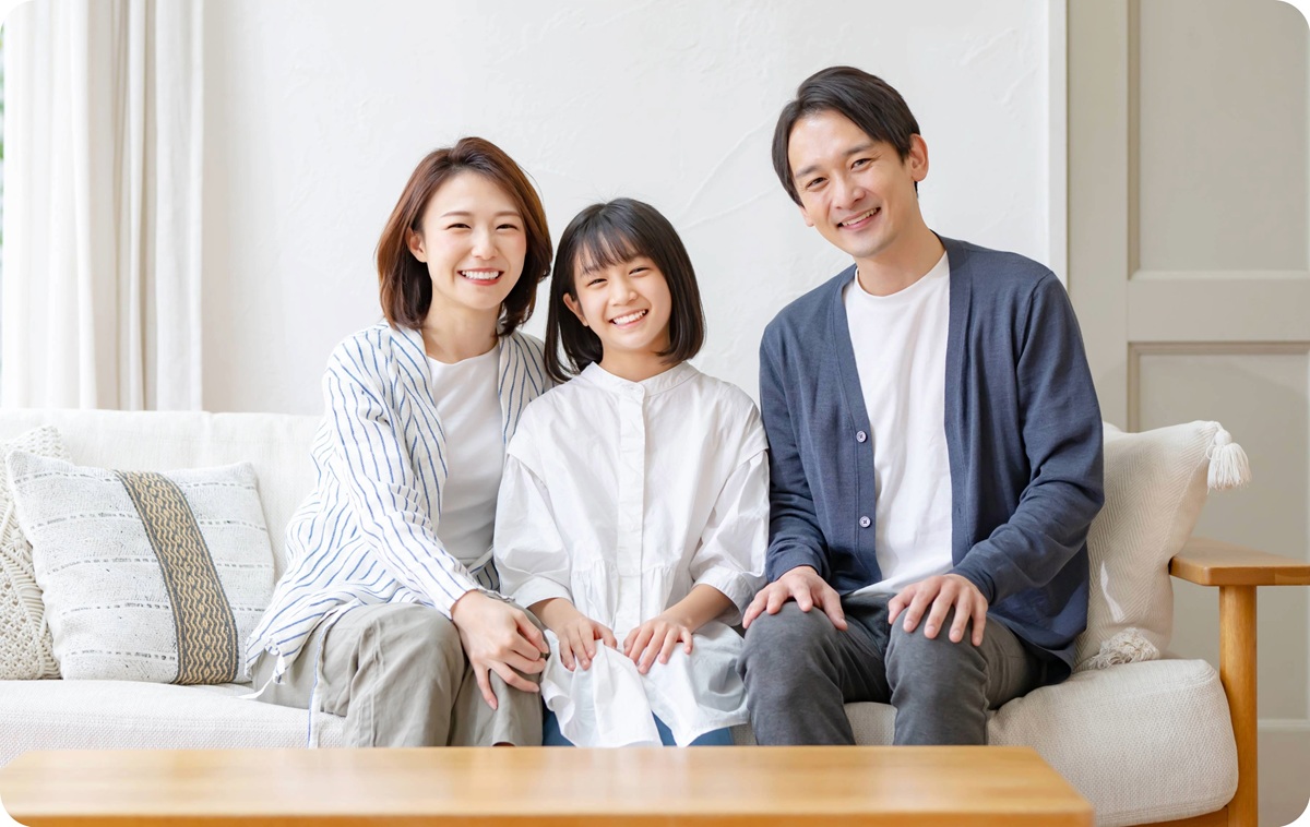 自宅のソファで笑顔で座る家族(両親と娘)