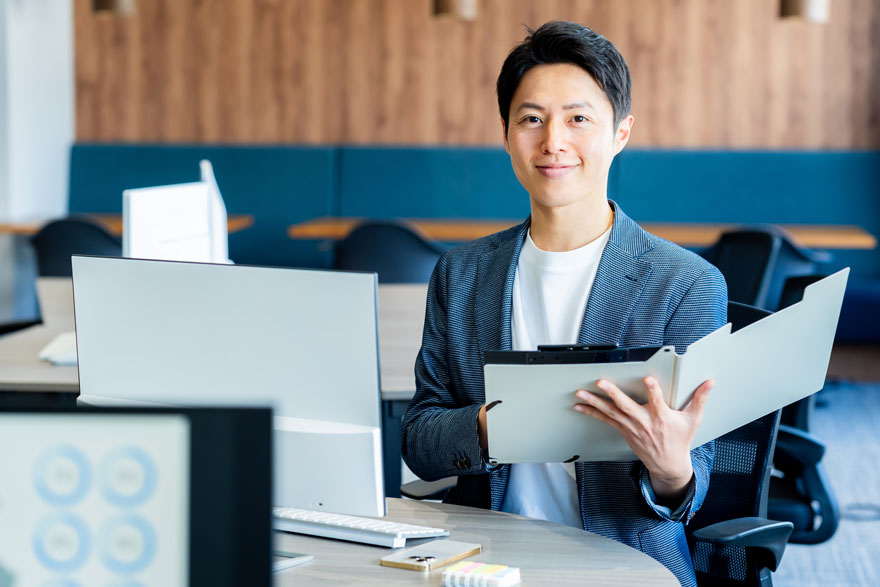 パソコンの前でファイルを広げる男性